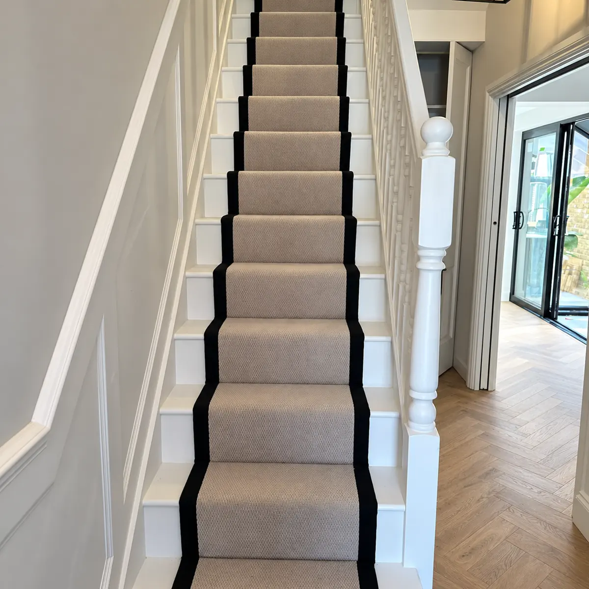 A neutral woven stair runner with contrasting black borders and white balustrades.