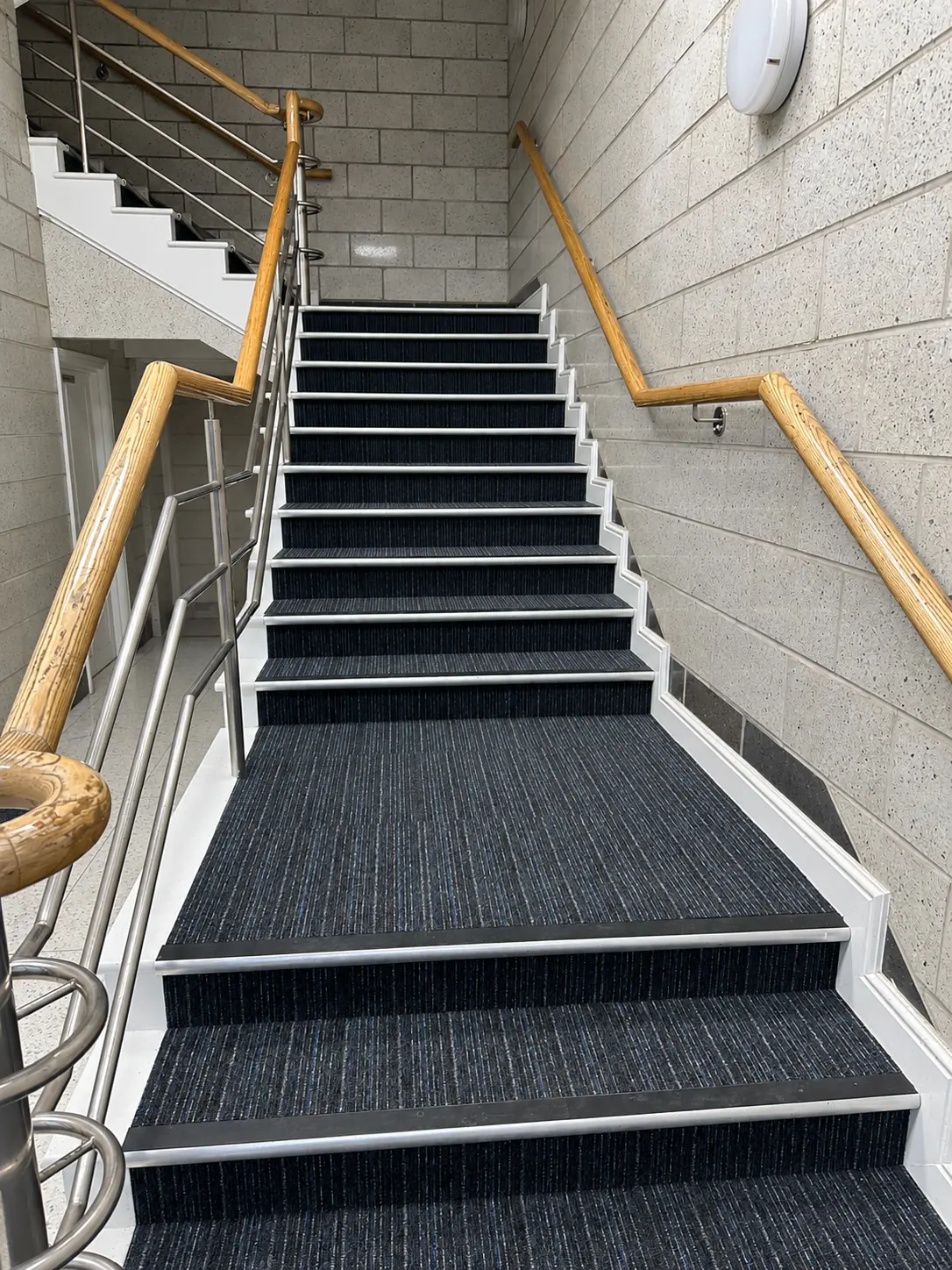 Communal hallway, landing and stair flooring with anti-slip stair nosings. Blue striped carpet and metal stair-edge profiles.